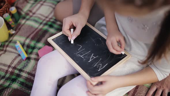 A Little Girl Learns to Write Words on the Blackboard with Chalk