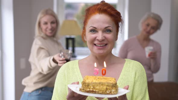 Front View Happy Woman Blowing Out Candles on Cake Making Wish Looking at Camera Smiling alt