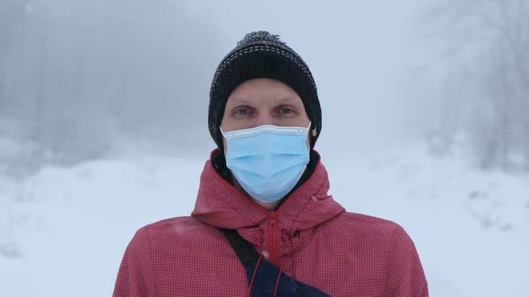 Young Man in Surgical Mask Looking at the Camera on a Snowy Background with Snowflakes Surround
