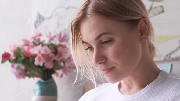 Close-up portrait of woman with light hair, she is in the office and reading a book at home, smiling