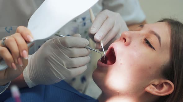 The girl at the dentist office shows sick teeth while looking in the mirror. alt