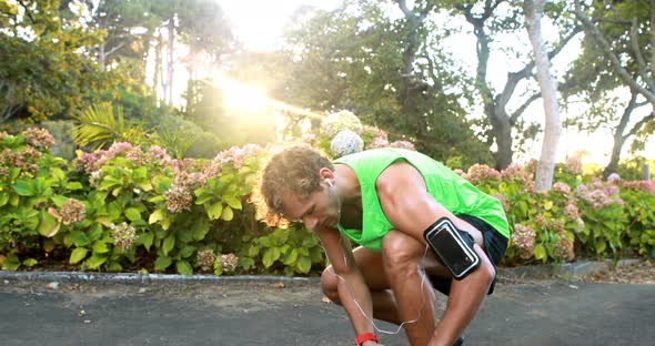 Man tying his shoe laces while jogging in park alt