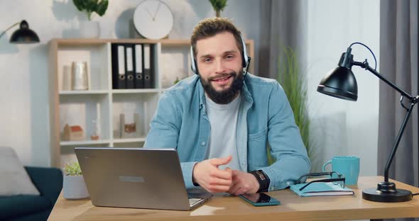 Bearded Guy in Headset Showing Sign Like Into Camera Sitting at the Desk in Home Office alt