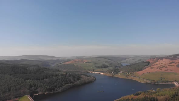 Drone travelling rising with Lady Bower Reservoir in view from Bamford Edge in the Peak District sho alt