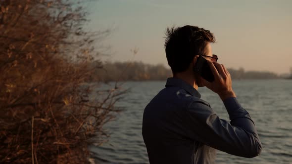 Man Talking By Smartphone Among Pond And Looking To Distance.Businessman At River Beach Using Mobil alt