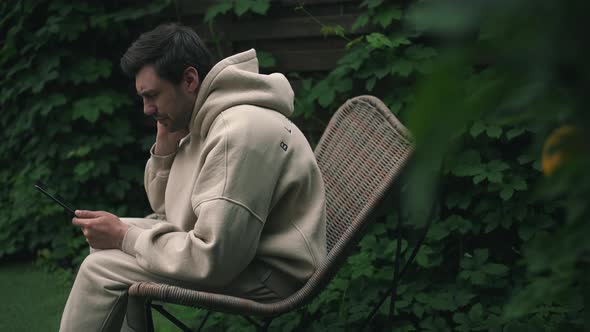 Man Felt Neck Pain While Sitting in the Garden with Tablet alt