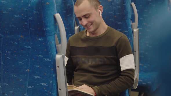 A Young Man Laughs While Reading a Book on the Train