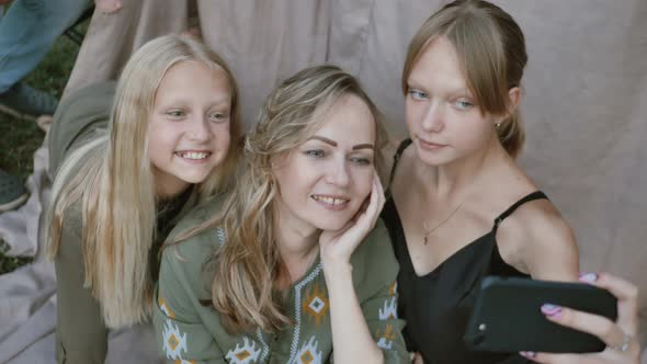 Close up of smiling mother with daughters makes funny selfies on the smartphone, grimacing alt
