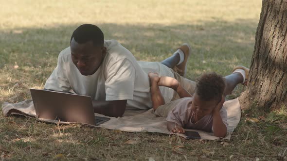 Man with Son Video Conferencing on Laptop in Park alt