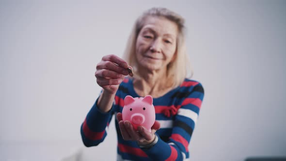Elderly Retired Woman Inserting Coins Into the Piggy Bank alt