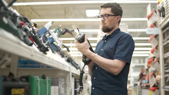 Male Customer is Checking a Hammer in a Shop of Building Tools alt