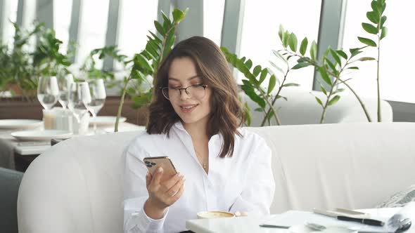 Business Woman Sitting in Coffee Shop During Free Time and Working on Smartphone