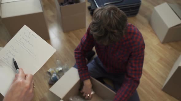 Young Couple Collects Things in a Box for Moving to a New Apartment