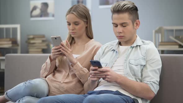 Couple in Love Indifferently Sitting on Couch Looking at Their Smartphones alt