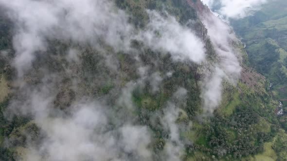 High mountainside in clouds, slow tilt up aerial shot alt