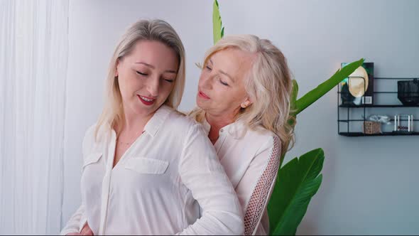 One Woman with Wavy Blonde Hair Standing in the Back Hugging Another Middleaged Caucasian Woman alt
