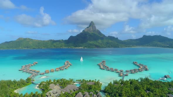 Aerial drone view of a luxury resort, overwater bungalows and sailboat in Bora Bora tropical island alt