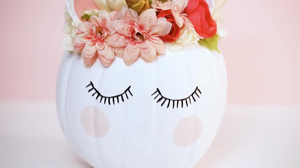 Craft pumpkin painted white and decorated with pink flowers as unicorn on pink background. alt