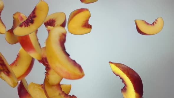 Fresh Ripe Peach Slices are Falling and Spinning on the White Background alt