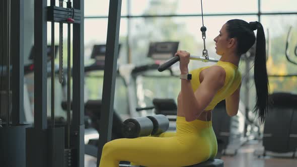 A Young Brunette Woman in a Yellow Suit is Doing Exercises for the Muscles of the Back on the alt