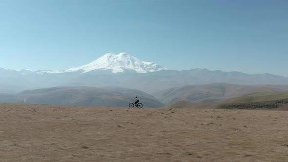 Bicycle Woman Riding Bike on Snowy Mountain Peak Background. Tourist Girl Traveling on Sport Enduro alt