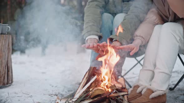 Man and Woman Warming Their Hands By a Campfire in the Woods in Winter