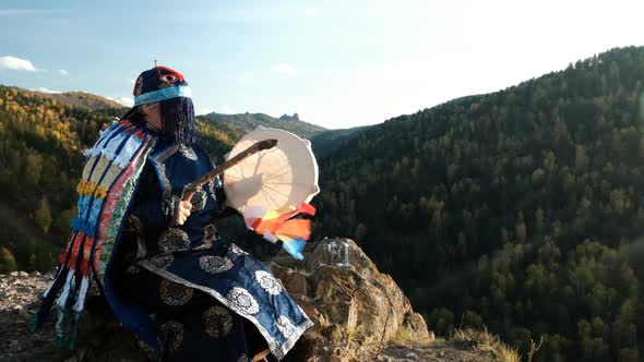 A Shaman Knocks on a Tambourine Sitting on a Rock on Top of a Mountain.