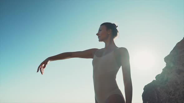 Dancing Ballerina Among Rocks Near Ocean or Sea at Sunrise or Sunset. Portrait of Flexible Woman alt