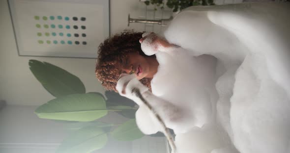 A Funny Woman Sits in a Tub Filled with Foam Holding a Shower and Singing Songs
