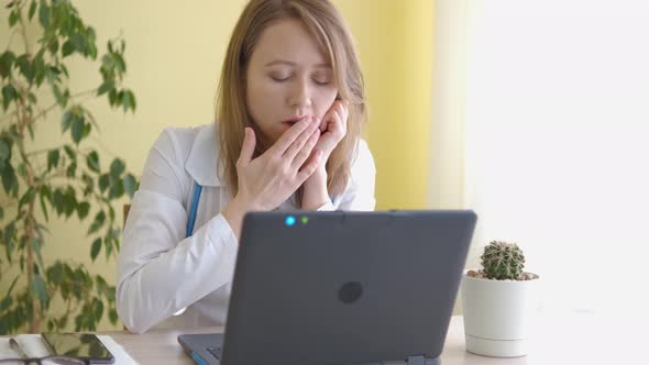 A nurse in a white coat is sleeping behind a laptop alt