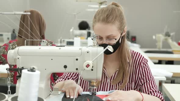 seamstress woman protective mask uses sewing machine when creating new clothes alt