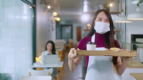 Attractive asian female cafe worker wears face mask and gloves giving takeaway food alt