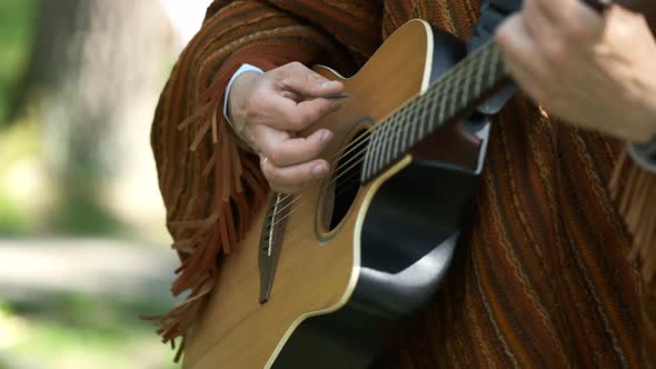 A man in a Mexican suit plays an acoustic guitar. Hands close-up.