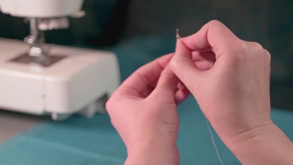 Tailor's hands inserting a thread into a needle. Repair of clothes at home.