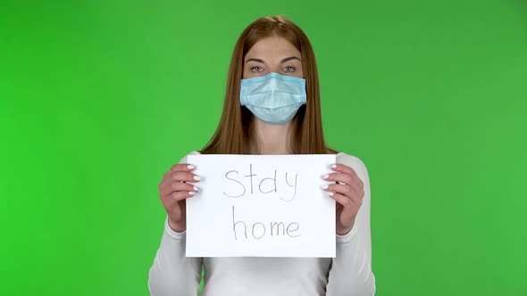 Portrait of Young Girl in Medical Protective Face Mask Looking at Camera and Holding a Poster with alt