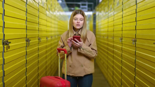 Positive Joyful Young Woman Using Smartphone App Looking Away and Leaving with Luggage in Self alt