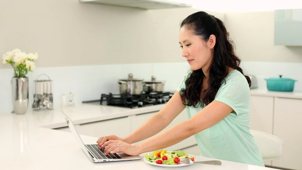 Smiling Woman Using Laptop And Eating Salad