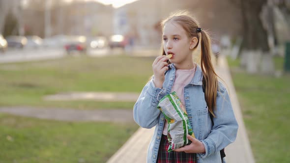 Young School Girl Eating Chips From Packet on Street alt