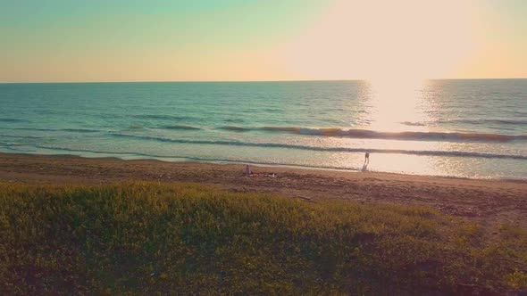 A guy and a woman are walking along a deserted beach, in the surf. alt