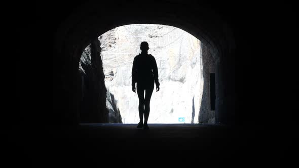 Camera Follows a Woman Silhouette Walking Through Dark Tunnel Towards the Light Raising Arms in Air alt