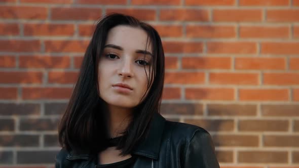 Portrait of a Young Sexy Woman Standing at a Brick Wall Walking Around the City at Sunset. alt