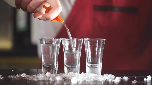 Expert Barman in Elegant Uniform Pouring Vodka in Frosted Short Glasses alt