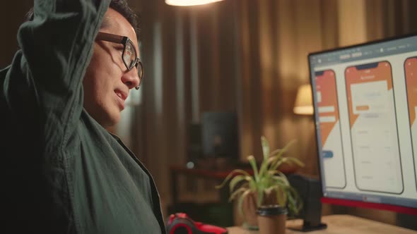 Asian Male Mobile Application Developer Stretching While Works With Graphics On Computer alt