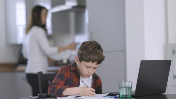 Boy doing homework while mother is cooking in background