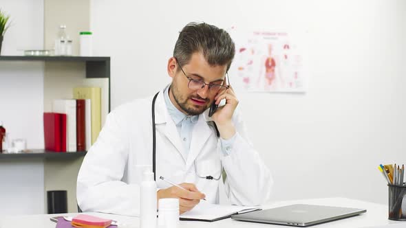 Doctor Talking on Phone with Patient and Writing Down the Symptoms alt