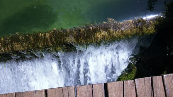 Pan of water flowing over edge with plants on it under wooden bridge alt