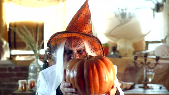 Old Man Ready for Halloween Party. Evil Wizard Hold Orange Pumpkin. Mature Man Magician in Witch Hat alt