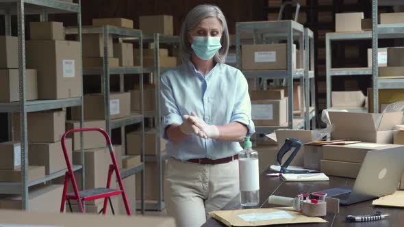 Mature Female Warehouse Worker Wearing Mask Using Sanitizer at Work alt