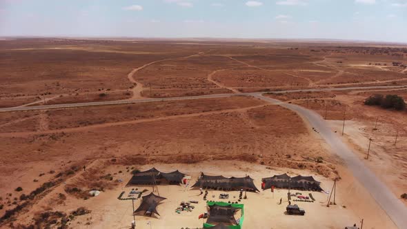 aerial shot of army camp of tents in the middle of the endless desert next to an empty road camera s alt