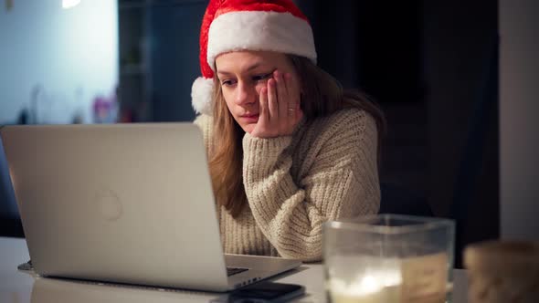 A Young Woman Wearing a Santa Hat Works Hard on a Laptop From Home alt